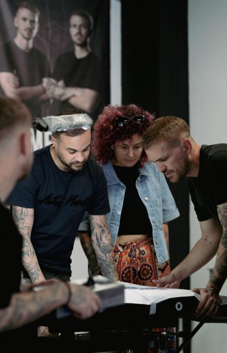 Profesores corrigiendo a alumnos del curso de tatuaje en la mesa de prácticas de Origen Tattoo Academy